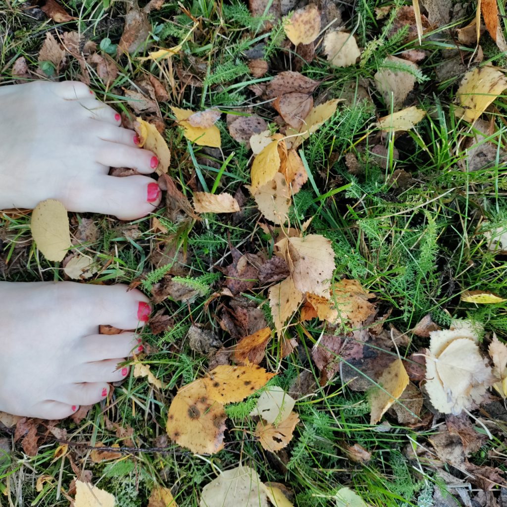 Paljaat jalat syksyn lehtien joukossa.