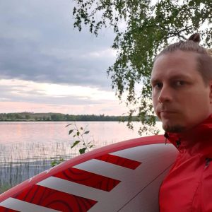 Mies rannalla ka purjelauta, taustalla järvimaisema