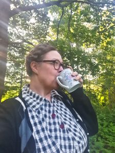 Nainen juo kahvia ulkona metsässä.