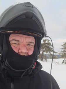 Mies talvivarusteissa lähikuvassa, taustalla luminen metsämaisema ja taivas