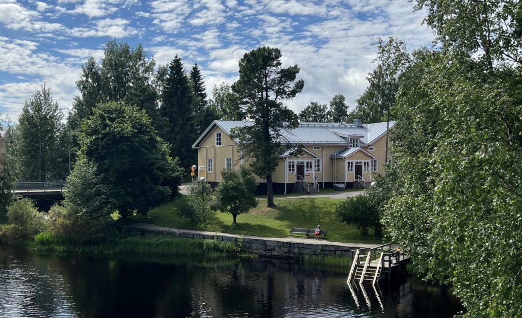 Keltainen puutalo joenrannalla aurinkosena kesäpäivänä