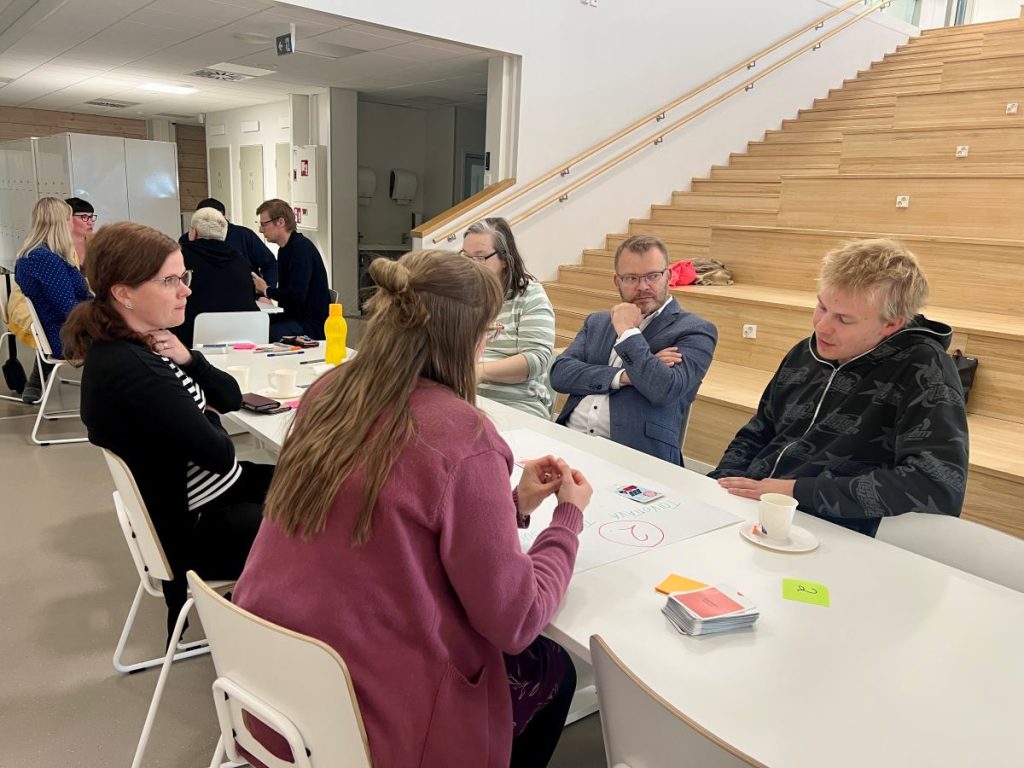 Ihmisiä keskustelemassa pöydän äärellä Karstulan yhtenäiskoulun ruokasalissa