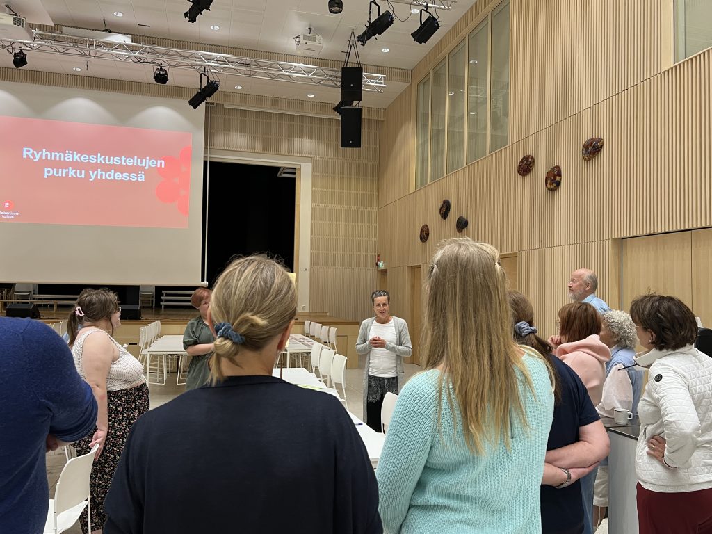 Ryhmä kaikenikäisiä ihmisiä selkä kameraan päin kuuntelemassa puheenvuoroa Saarijärven koulu- ja kulttuurikeskuksessa