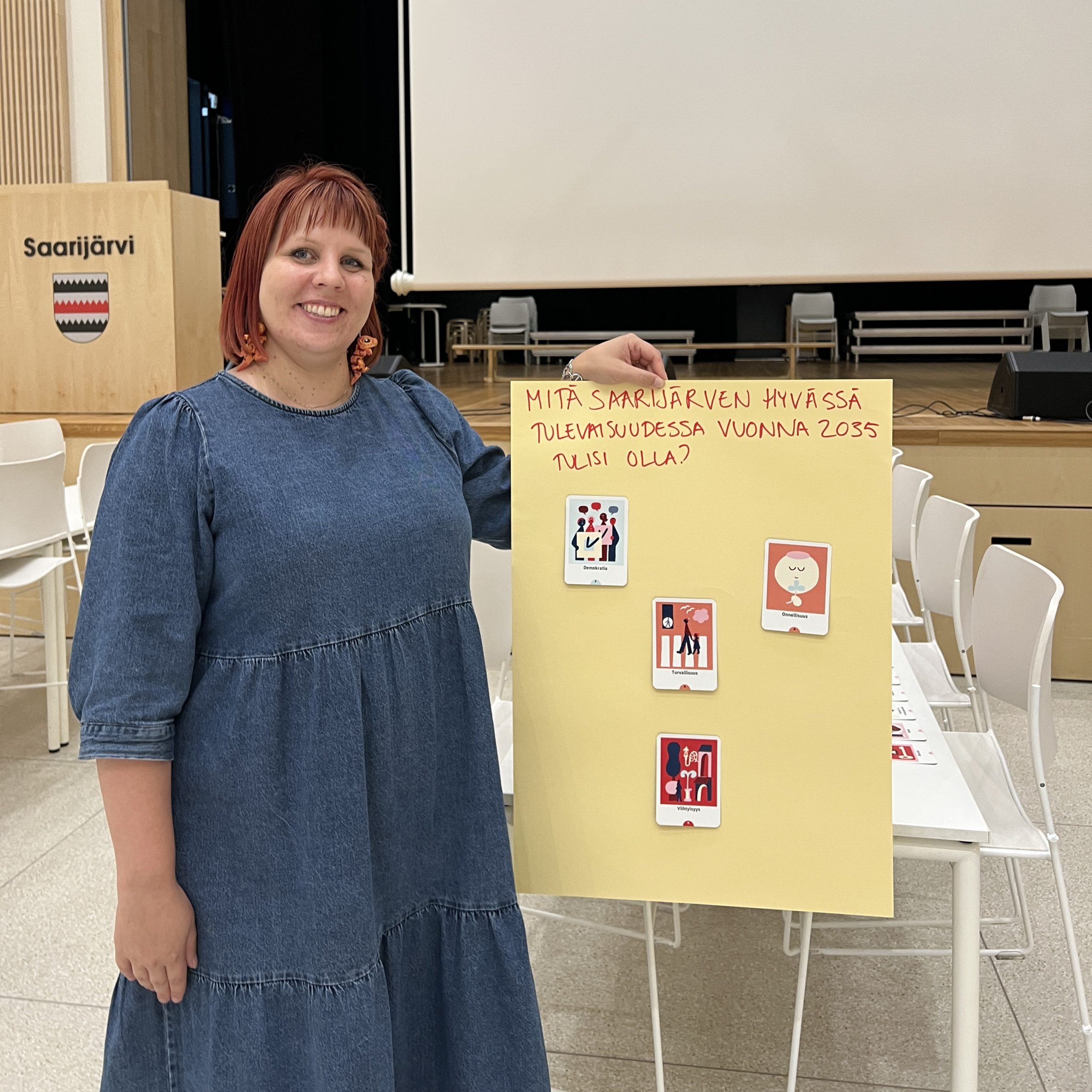 Nuorehko nainen näyttää tulevaisuuskorteista muodostettua tulevaisuusseinää ja hymyilee.