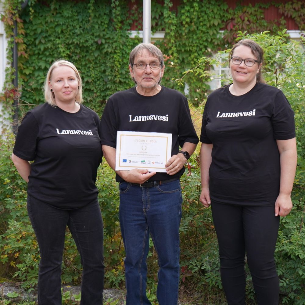 Kaksi naista ja yksi mies pitelevät käsissään diplomia ja katsvat kameraan vehreällä pihalla.