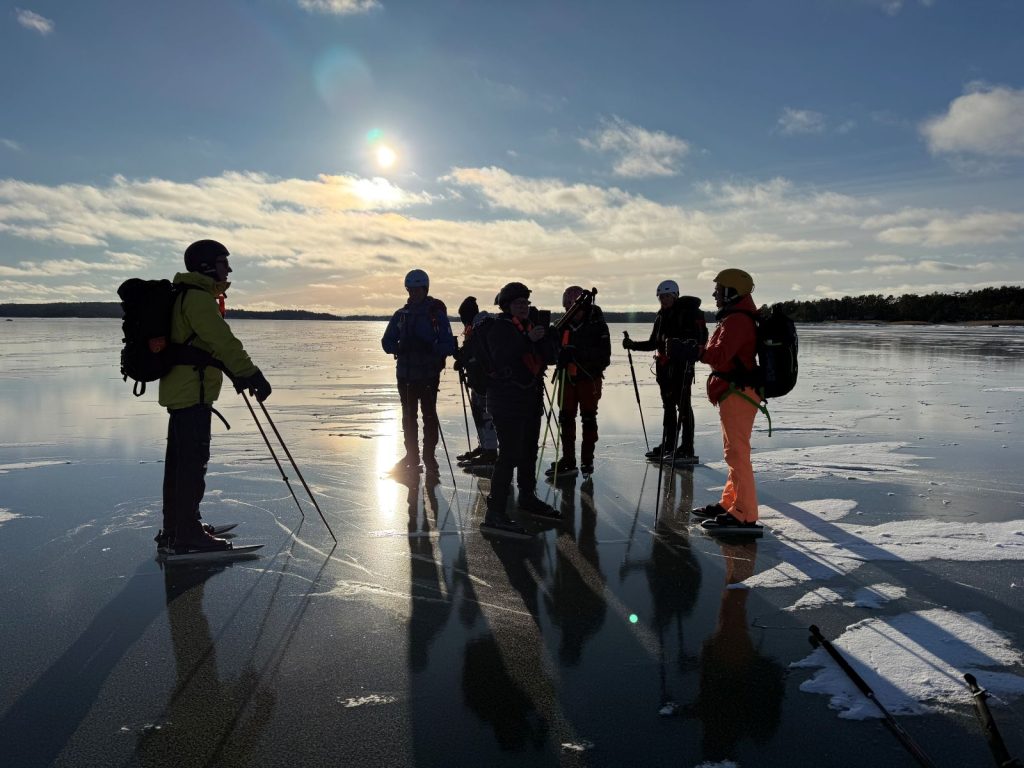 Ihmisiä auringonpaisteessa peilikirkkaalla jäällä Ahvenanmaalla retkiluistimet jalassa