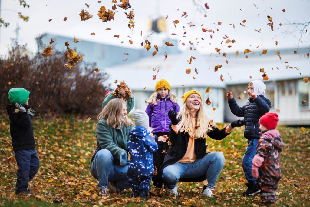 Lapsia ja kaksi äitiä heittelemässä syksyllä puista pudonneita lehtiä Ahvenanmaalla.